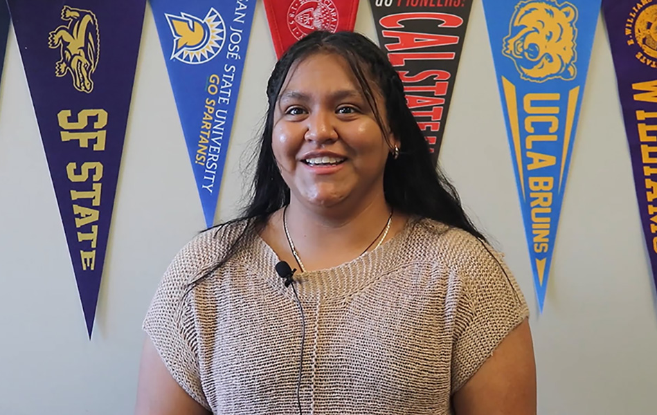Student smiling at the camera, with a variety of college banners in the background